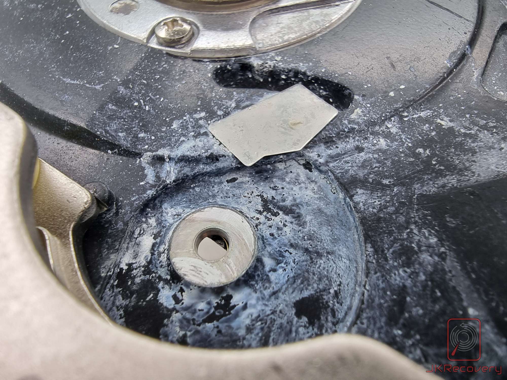 Zbliżenie na uszkodzony silnik wrzeciona dysku twardego HDD z widocznymi śladami korozji, białymi osadami i odłamanym fragmentem metalu wokół piasty wirnika
